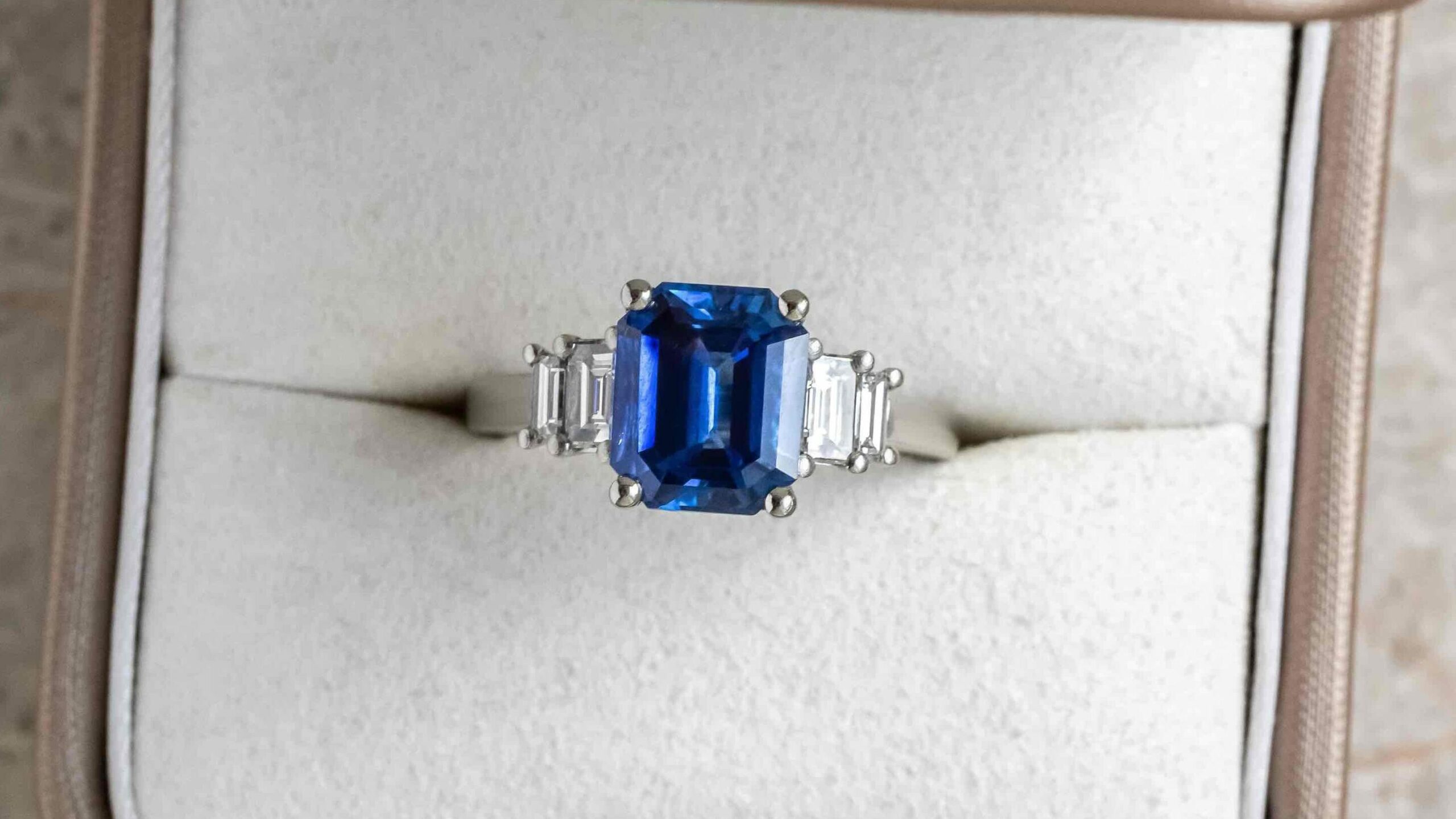 platinum engagement in in a box featuring a blue sapphire gemstone and diamonds for sidestones