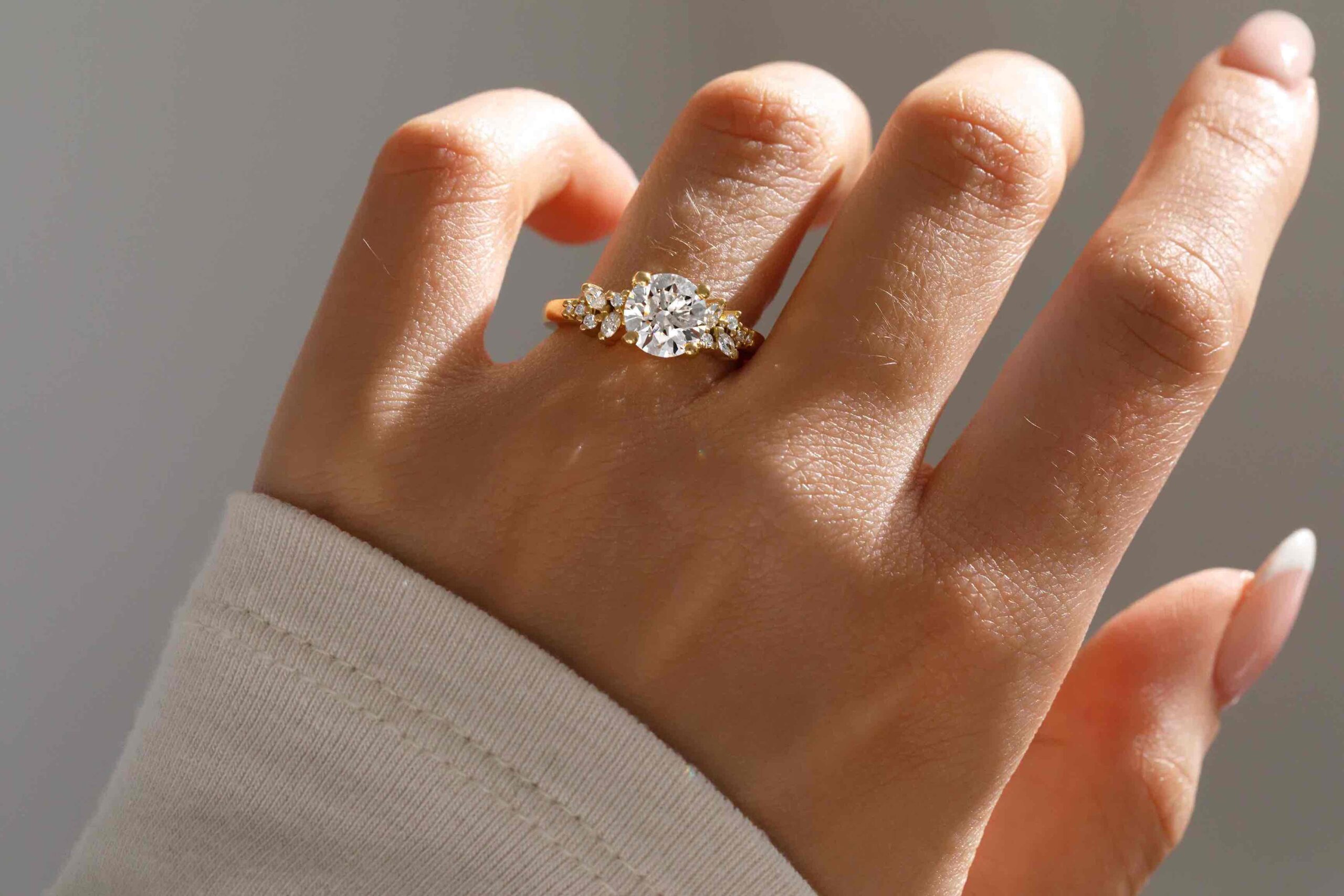 hand wearing an 18k yellow gold cluster style engagement ring featuring lab grown marquise side diamonds and a lab grown round diamond