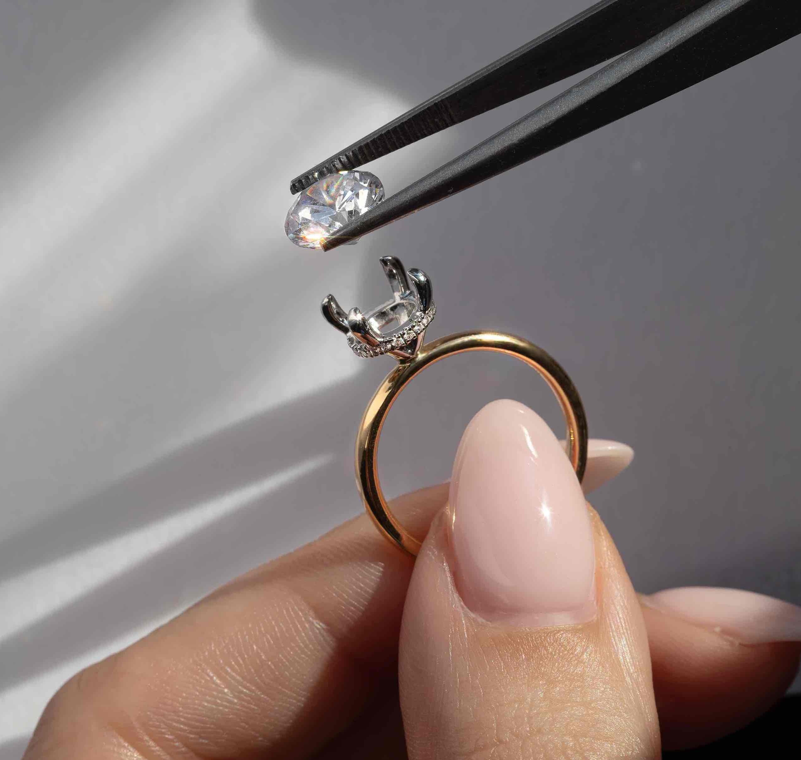 Lab grown diamond being placed in a 2 tone solitaire engagement ring mount that features a hidden halo